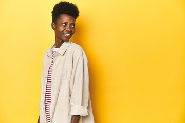 Obraz na płótnie Canvas African woman, beige shirt, red striped tee, yellow studio, looks aside smiling, cheerful and pleasant.