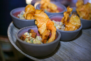 Ceviche de peixe com cubos de abóbora e chips de batata doce, servido em um bowl de cerâmica artesanal.