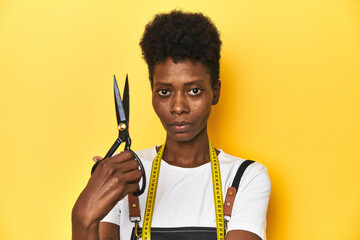 African tailor woman with scissors, yellow studio background.