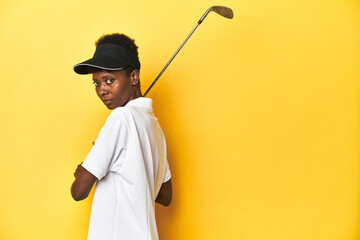 African woman golfer preparing to swing at ball, yellow studio background.