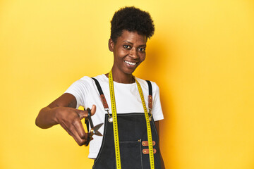 African tailor woman with scissors, yellow studio background.