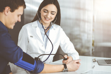 Fototapeta premium Young woman-doctor is checking her patient's blood pressure, while sitting together in clinic. Medicine and healthcare concepts