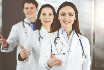 Fototapeta premium Doctors are standing as a team while offering their helping hands for shaking hand or saving people's life. Medical help, insurance in health care, best disease treatment and medicine concept