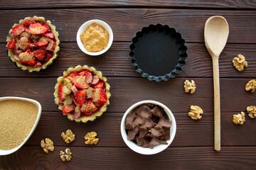 Mini tarts with strawberry, chocolate and nuts preparation on brown wooden table, top view. 