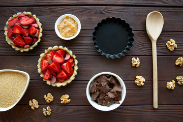 Mini tarts with strawberry, chocolate and nuts preparation on brown wooden table, top view. 