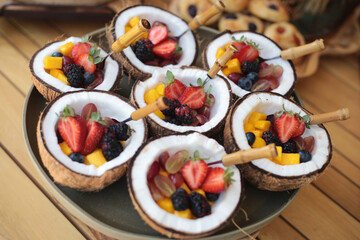 Salada de frutas servida em tigelas de coco, acompanhada por um garfo requintado de cabo de bambu, em um evento social chique.