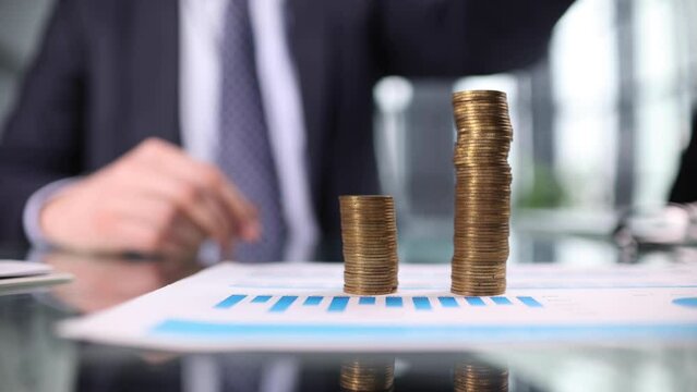 Man puts a coin on a stack of coins on the table