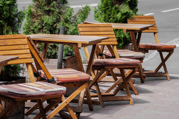 Fototapeta na wymiar Tourist season. Summer vacation. A warm day. Cozy street cafe. A row of empty wooden tables and chairs. Awaiting clients.