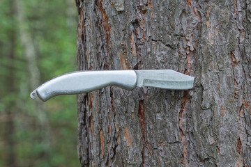 one white iron folding knife sticks out in the gray bark of a pine tree outdoors in nature