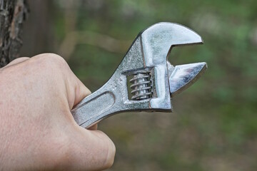 a hand holds one gray iron adjustable wrench outdoors on a green background