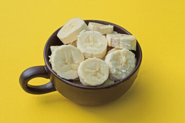 white pieces of fresh raw sliced bananas in a brown ceramic cup on a yellow table