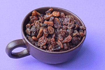 a bunch of brown dry raisins in a cup stands on a lilac table