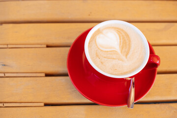 Obraz premium Red cup, Latte coffee heart-shaped on wooden table backdrop or background, Concept For relaxing