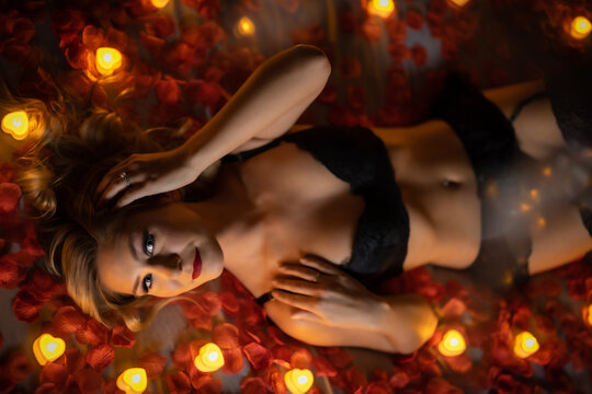 blonde female posing on rose pedal covered bed with dozens of candle lights