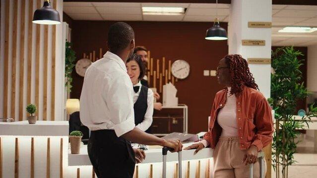 Husband and wife on honeymoon trip requesting special room amenities from asian receptionist in hotel lobby. Helpful concierge personnel presenting holiday package deal to couple in luxury resort