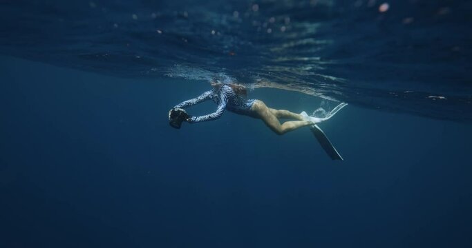 Underwater photographer. Man slowly swim underwater with professional camera housing in freshwater beautiful woman floats under water dark background, girl swims to surface of water, creating bubbles