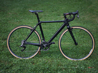 black carbon bicycle in field of grass (road bike with drop handlebars, skinwall tires) cyclocross...