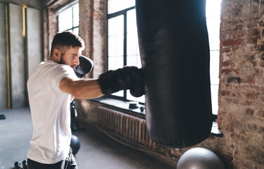 Male boxer punching bag in gym with boxing gloves