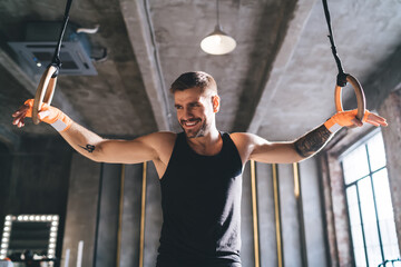 Strong male athlete standing with gymnastic rings in gym