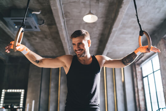 Strong male athlete standing with gymnastic rings in gym