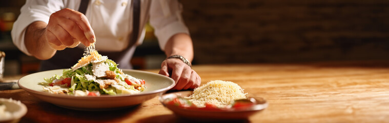 Chef topping a Caesar Salad with Parmesan cheese on a wooden table. Copy space. Gastronomy concept. AI Generative