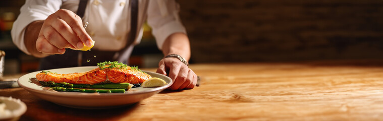 Chef using lemon to season a dish of salmon, asparagus, and aromatic herbs on a wooden table with space for text. Copy space. Gastronomy concept. AI Generative