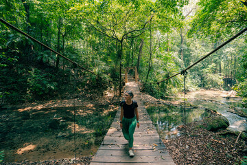 a girl walks on a suspension bridge in a tropical forest