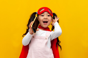 little asian girl in superman costume and mask is talking on the phone, korean child in cape