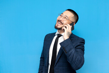successful asian businessman in suit and glasses on blue isolated background is talking on the phone