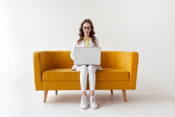 young businesswoman in suit sits on comfortable soft sofa and uses laptop, girl in formal wear is typing on computer