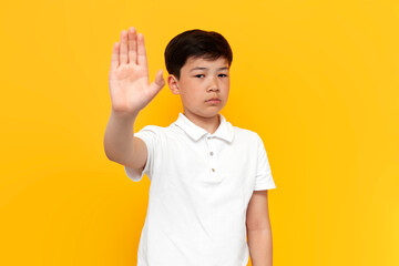 little asian boy showing palm and stop gesture on yellow background, korean child showing refusal