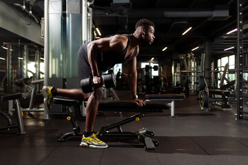 Fototapeta na wymiar athletic african american man trains in dark gym, athletic guy lifts heavy dumbbells in fitness club