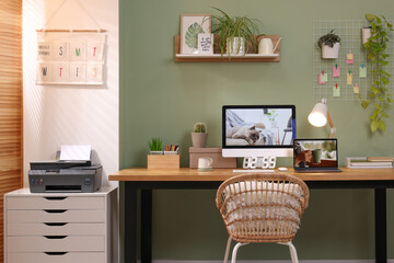 Fototapeta premium Stylish workplace with computer, laptop and lamp near olive wall at home