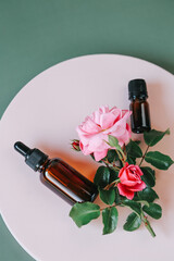 Obraz na płótnie Canvas Rose water.Rose oil in a glass bottle on a pink podium on a gray background. View from above .Aromatherapy and cosmetics.Organic natural rose oil.