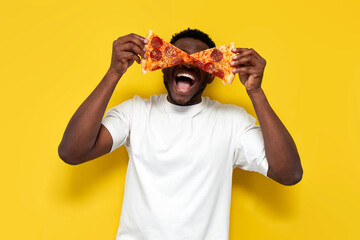 joyful african american man in white t-shirt holds two pieces of pizza in front of his eyes and...