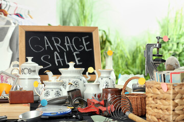 Blackboard with sign Garage Sale and many different stuff on black wooden table indoors