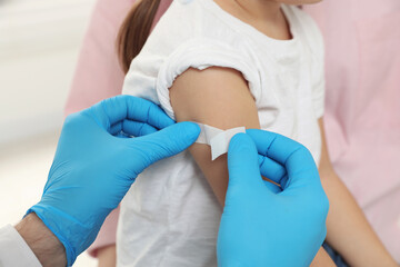 Fototapeta premium Children's hepatitis vaccination. Mother with her daughter. Doctor sticking medical plaster on little girl's arm, closeup