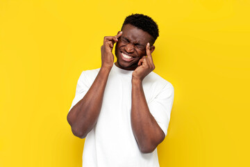 unhappy african american man in white t-shirt suffers from headache and fatigue on yellow background