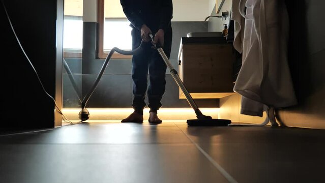 Bathroom cleaning.Man cleaning the room. Vacuum cleaner in the bathroom. The man is vacuuming in a dark bathroom with lighting. 4k footage