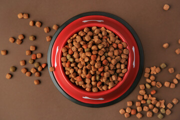Dry dog food and feeding bowl on brown background, flat lay