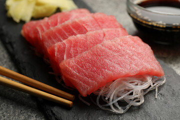 Tasty sashimi (pieces of fresh raw tuna), glass noodles and chopsticks on black board, closeup