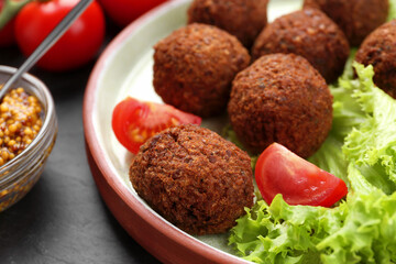 Delicious falafel balls, tomatoes and lettuce on dark table, closeup. Vegan meat products