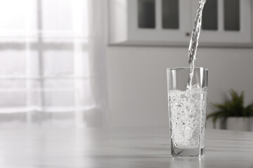 Pouring water into glass at table indoors, space for text