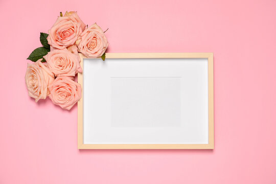 Empty photo frame and beautiful roses on pink background, flat lay. Mockup for design