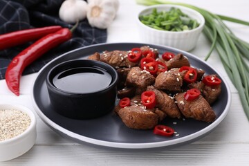Plate with tasty soy sauce and roasted meat on white wooden table, closeup