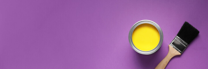 Can with yellow paint and brush on purple background, flat lay. Banner design with space for text