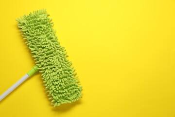 Mop with plastic handle on yellow background, top view. Space for text