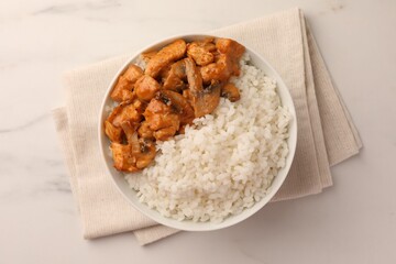 Bowl of delicious rice with meat and mushrooms on white marble table, top view