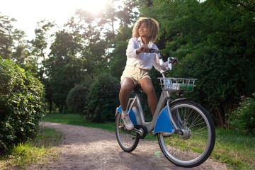 young african american girl rides bicycle in the park and smiles, curly woman actively rests and travels by bicycle