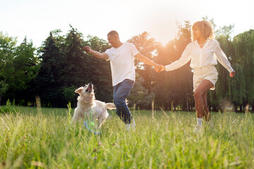 young african american couple play with dog in park on green grass and run